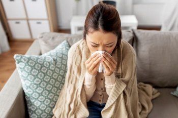 healthcare, cold and people concept - sick asian woman in blanket taking paper tissue from box and blowing her nose at home. sick woman blowing nose in paper tissue at home