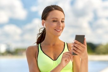fitness, sport and healthy lifestyle concept - happy smiling young woman with earphones and smartphone exercising outdoors. woman with earphones and smartphone doing sports