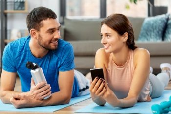 fitness, sport and technology concept - happy couple with smartphone having break at home. happy couple with smartphone after sports at home