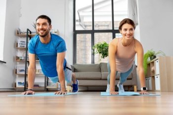 sport, fitness, lifestyle and people concept - smiling man and woman exercising and doing plank at home. happy couple exercising at home
