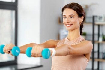 fitness, sport and healthy lifestyle concept - happy woman with dumbbells exercising at home. happy woman with dumbbells exercising at home