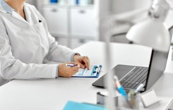 medicine, healthcare and profession concept - female doctor in white coat with laptop computer and medical report at hospital. doctor with laptop and medical report at hospital