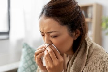 healthcare, cold and people concept - sick asian woman in blanket taking paper tissue from box and blowing her nose at home. sick woman blowing nose in paper tissue at home