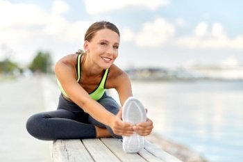 fitness, sport and healthy lifestyle concept - happy smiling young woman stretching leg on bench outdoors. happy young woman doing sports and stretching leg
