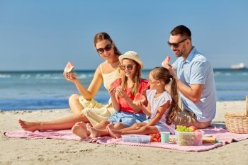 family, leisure and people concept - happy mother, father and two daughters having picnic on summer beach and eating watermelon. happy family having picnic on summer beach