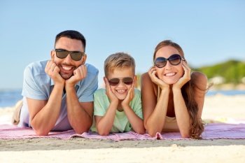 family, leisure and people concept - happy mother, father and little son in sunglasses lying on summer beach. happy family lying on summer beach
