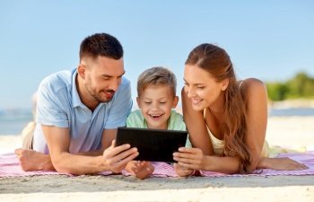 family, leisure and people concept - happy mother, father and son with tablet pc computer laying on summer beach. happy family with tablet computer on summer beach