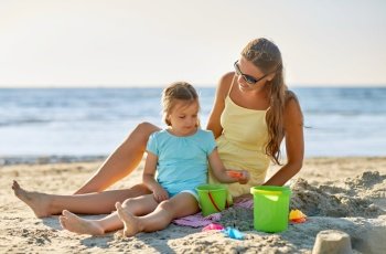 family, leisure and people concept - mother and daughter playing with sand toys on summer beach. mother and daughter playing with toys on beach