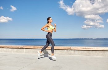 fitness, sport and healthy lifestyle concept - young woman running along sea promenade. young woman running along sea promenade