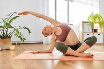 sport, fitness and pregnancy concept - happy smiling pregnant woman doing yoga exercise on mat at home. happy pregnant woman doing yoga at home