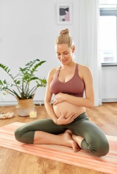 yoga, pregnancy and people concept - happy pregnant woman sitting on exercise mat at home. happy pregnant woman doing yoga at home