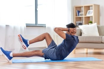 sport, fitness and healthy lifestyle concept - indian man making abdominal exercises at home. indian man making abdominal exercises at home