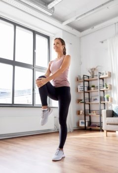 sport, fitness and healthy lifestyle concept - smiling young woman stretching leg at home. smiling young woman stretching leg at home
