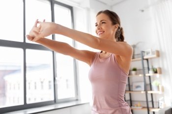 sport, fitness and healthy lifestyle concept - smiling young woman stretching arms at home. smiling young woman stretching arms at home