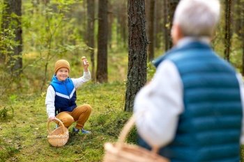 picking season, leisure and people concept - happy smiling grandson with basket showing mushroom to his grandmother in forest. grandmother and grandson with mushrooms in forest
