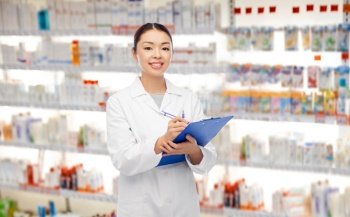 medicine, profession and healthcare concept - happy smiling asian female pharmacist or doctor with clipboard and pen over pharmacy background. happy asian female pharmacist with clipboard