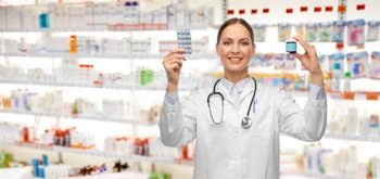 medicine, profession and healthcare concept - happy smiling female doctor with stethoscope comparing pills in jar and pack over pharmacy background. smiling female doctor holding medicine pills