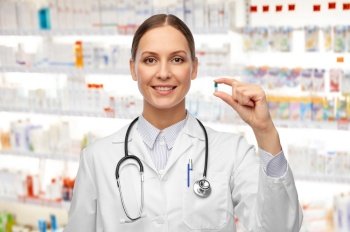 medicine, profession and healthcare concept - happy smiling female doctor with stethoscope holding pill over pharmacy background. female doctor holding medicine pill at pharmacy
