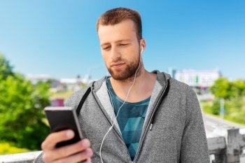 fitness, sport and technology concept - young man with earphones and smartphone listening to music outdoors. young man with earphones and smartphone