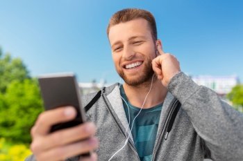 fitness, sport and technology concept - happy smiling young man with earphones and smartphone listening to music outdoors. smiling young man with earphones and smartphone