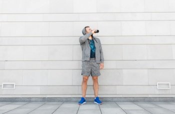 fitness, sport and people concept - young man with bottle drinking water in city. sportsman with bottle drinking water in city