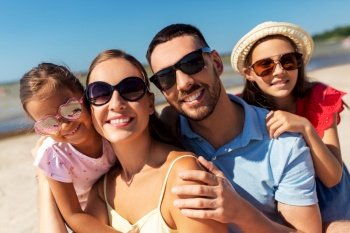 family, leisure and people concept - portrait of happy mother, father and two daughters in sunglasses on summer beach. happy family in sunglasses on summer beach
