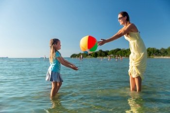 family, leisure and people concept - happy mother and little daughter playing inflatable ball on beach. mother and daughter playing with ball on beach