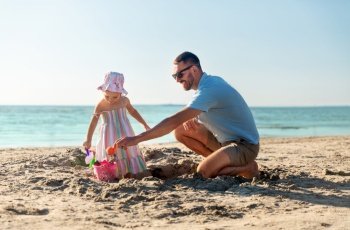 family, leisure and people concept - father and baby daughter playing with sand toys on summer beach. father and daughter playing with toys on beach