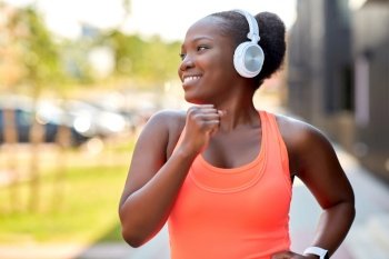 fitness, sport and healthy lifestyle concept - happy smiling young african american woman in headphones running in city. happy african woman in headphones running outdoors