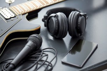 leisure, music and musical instruments concept - close up of bass guitar, smartphone, microphone and headphones on black table. close up of bass guitar and smartphone