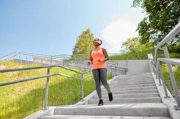fitness, sport and healthy lifestyle concept - happy smiling young african american woman in headphones downstairs at park. happy african woman in headphones running outdoors