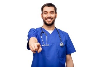 healthcare, profession and medicine concept - happy smiling doctor or male nurse in blue uniform with stethoscope pointing finger to camera over white background. smiling doctor or male nurse pointing to camera
