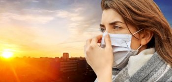 health, safety and pandemic concept - young woman wearing protective medical mask over sunset in city on background. young woman wearing protective medical mask