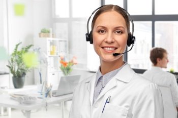 medicine, profession and healthcare concept - happy smiling female doctor with headset over medical office at hospital on background. smiling female doctor with headset at hospital