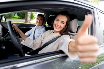 driver courses and people concept - car driving school instructor and young woman showing thumbs up to drive. car driving instructor and woman showing thumbs up