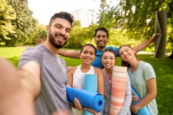 fitness, sport and healthy lifestyle concept - group of happy people with yoga mats taking selfie at park. people with yoga mats taking selfie at park