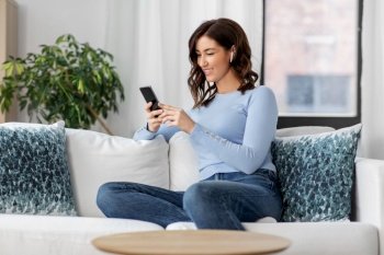 people, technology and leisure concept - happy young woman with wireless earphones and smartphone listening to music at home. woman with earphones and smartphone at home