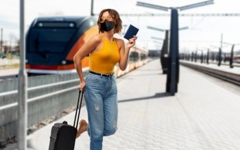 tourism, vacation and people concept - smiling young woman or teenage girl with travel bag and passport over train on railway station on background. woman in mask with travel bag over train
