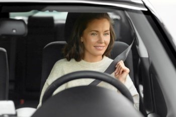 safety and people concept - happy smiling young woman or female car driver fastening seat belt. woman or female car driver fastening seat belt