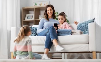 people, family and technology concept - happy mother and two daughters with smartphone at home. happy mother and daughters with smartphone at home