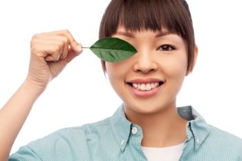eco living, environment and sustainability concept - portrait of happy smiling young asian woman in turquoise shirt holding green leaf over white background. smiling asian woman holding green leaf