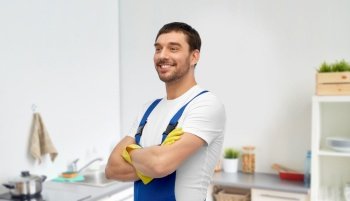 profession, cleaning service and plumbing concept - happy smiling male worker, plumber or cleaner in overall and gloves over home room background. happy male worker or cleaner in gloves at kitchen