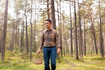 picking season and leisure people concept - happy smiling middle aged man with wicker basket of mushrooms walking in autumn forest. happy man with basket picking mushrooms in forest