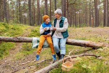 picking season, leisure and people concept - grandmother and grandson having picnic and drinking tea in autumn forest. grandmother with grandson drinking tea in forest