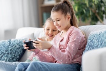 family, childhood and technology concept - two happy smiling little girls or sisters with smartphone at home. happy little girls or sisters with phone at home