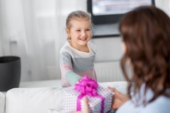 people, family and holidays concept - happy little daughter giving present to her mother at home. happy daughter giving present to mother at home
