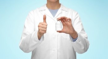 medicine, vaccination and healthcare concept - close up of female doctor or nurse with drug in bottle showing thumbs up over blue background. close up of doctor with medicine showing thumbs up
