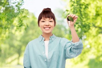 eco living, environment and sustainability concept - portrait of happy smiling young asian woman in turquoise shirt holding car key with green leaf over natural background. happy asian woman holding car key with green leaf