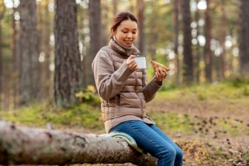 picking season, leisure and people concept - young asian woman drinking tea and eating sandwich in autumn forest. woman drinking tea and eating sandwich in forest