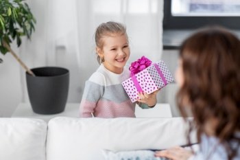 people, family and holidays concept - happy little daughter giving present to her mother at home. happy daughter giving present to mother at home